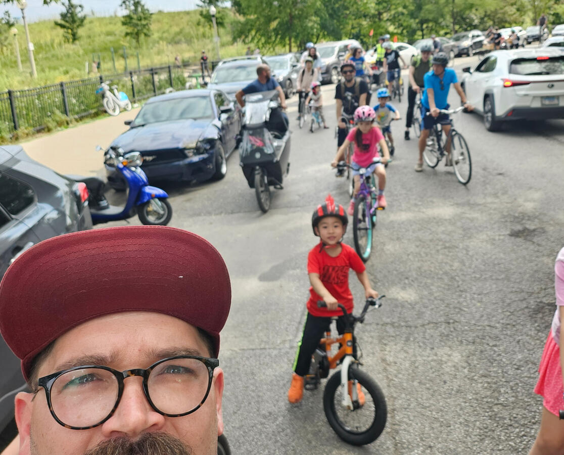 A selfie taken by a man on a bike with a growing column of kids on bikes in the background