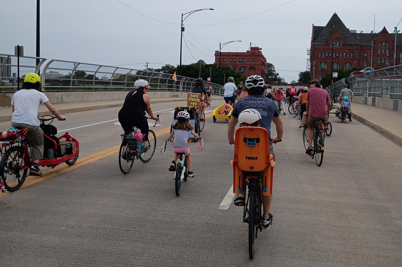 A mixed age group of bike riders shown from the rear going over the highway and train tracks on 31st St.